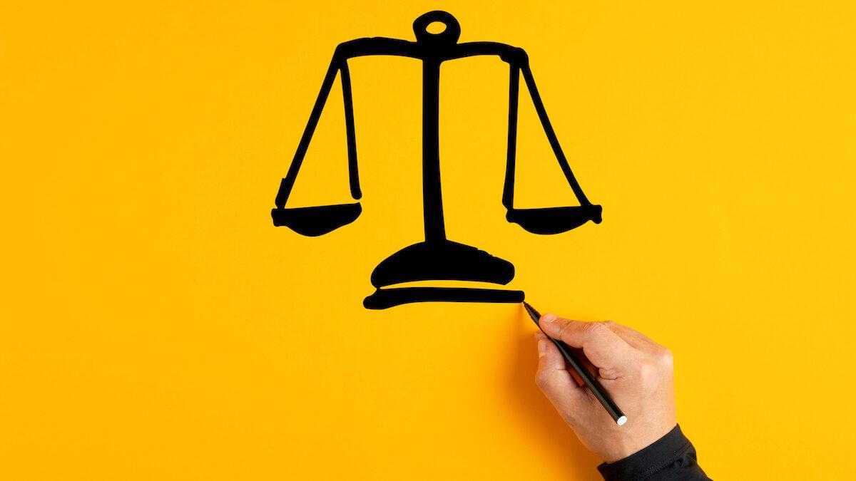 Male hand drawing a justice scale on yellow background. Fairness, equality or trust