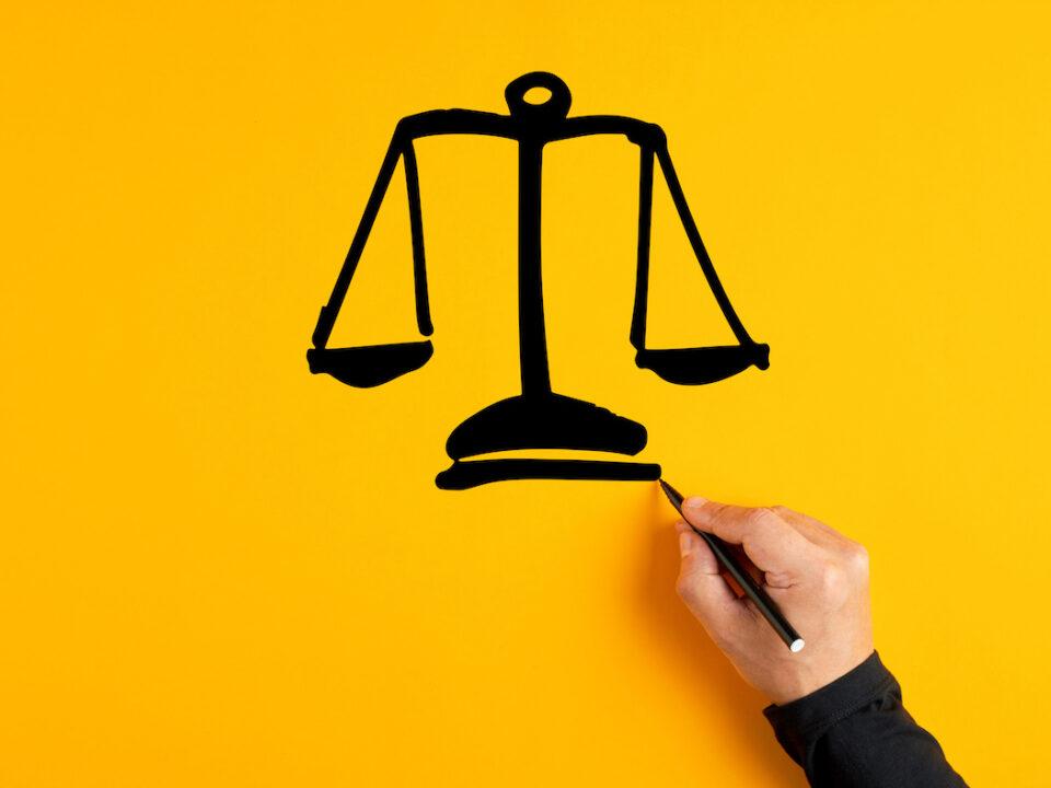 Male hand drawing a justice scale on yellow background. Fairness, equality or trust